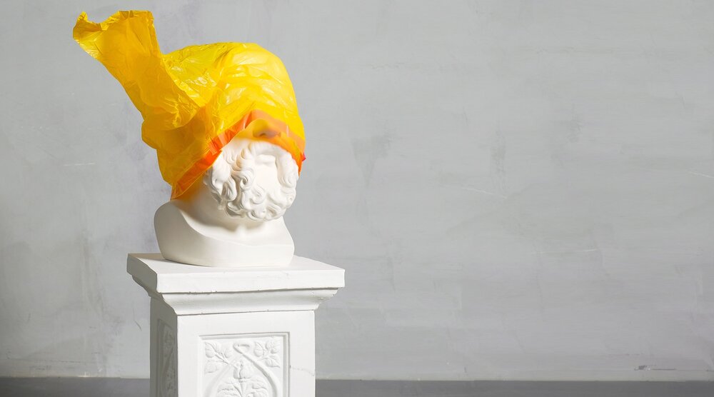 Eine Statue mit einer gelben Mülltüte auf dem Kopf.