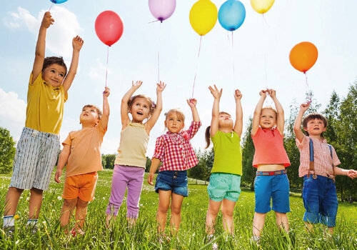 Sieben Kinder stehen auf einer Wiesen und lassen Luftballons steigen.
