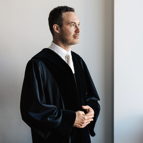 Portraitfoto von Richter in Robe, der zur Seite steht und blickt.
