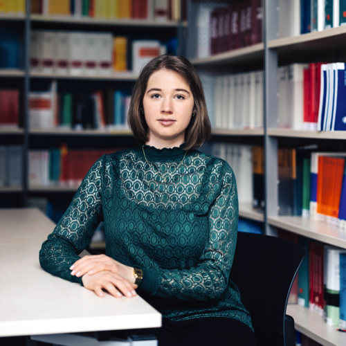 Junge Frau mit grünem Oberteil, die an einem Tisch in einer Bibliothek sitzt