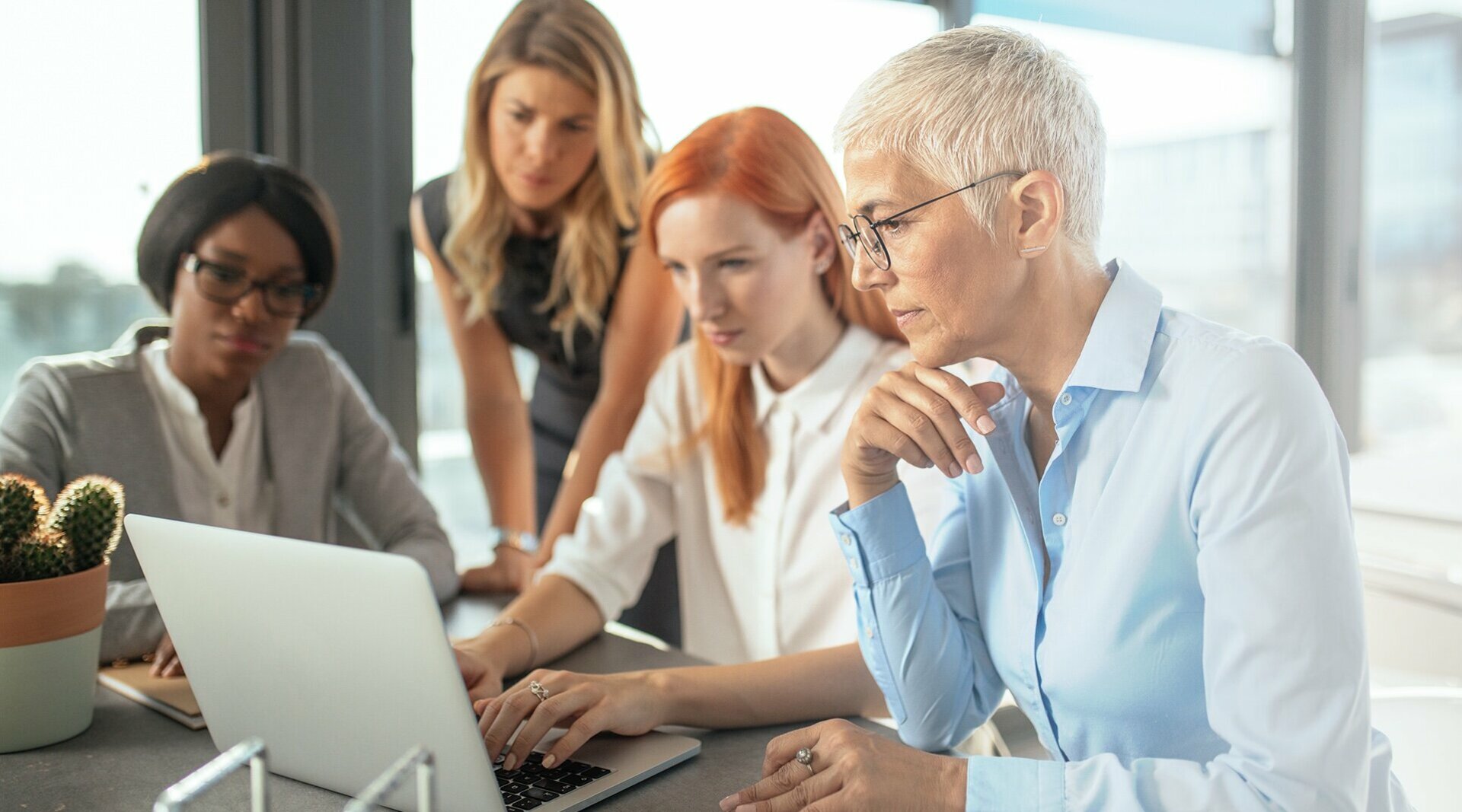 Zu sehen sind vier Frauen, die konzentriert an einem Laptop arbeiten.