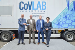 Klaus Weber, Prof. Dr. med. Michael Neumaier, Christoph Dahl und Marion Gentges stehen vor dem CovLAB. Klaus Weber hält ein Modell des CovLAB-Trucks in der Hand.
