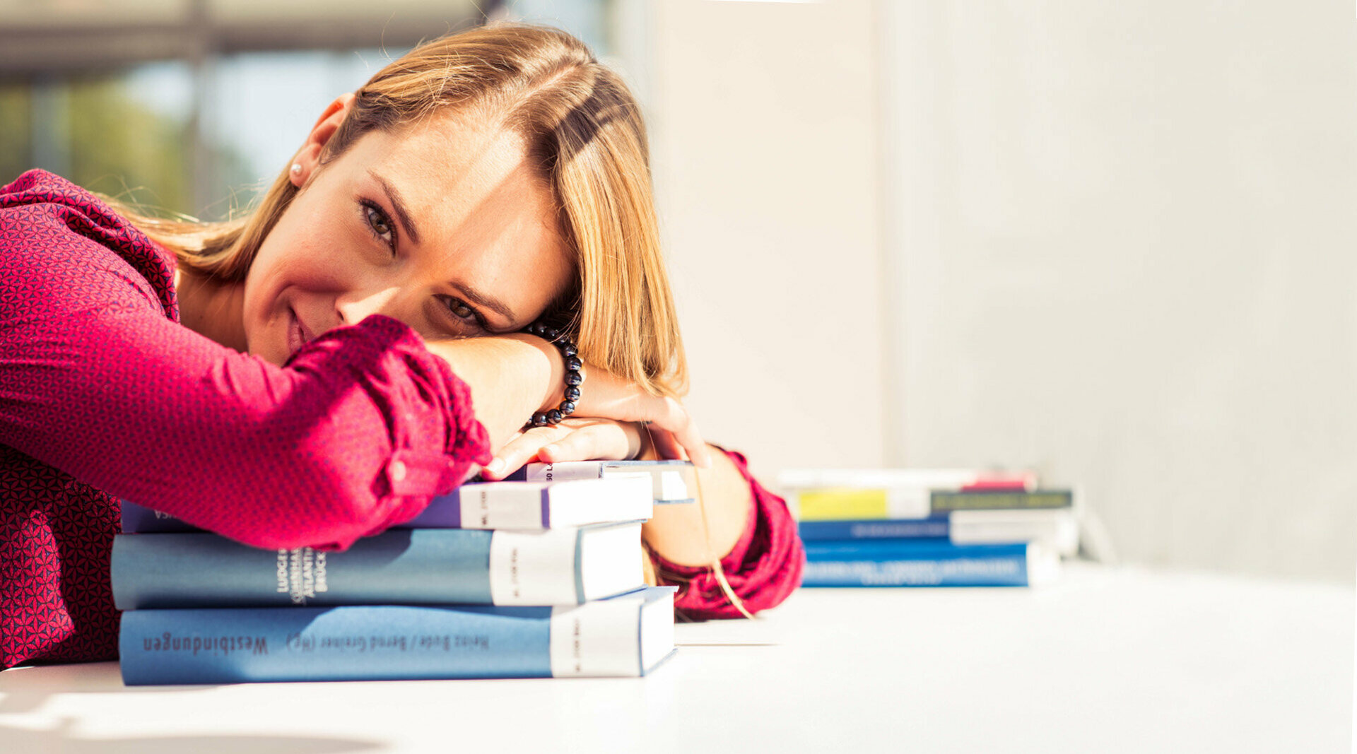 Eine junge Frau hat den Kopf auf einen Bücherstapel gelegt