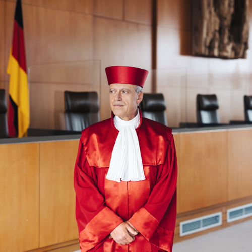 Richter des Bundesverfassungsgerichts in roter Robe im Gerichtssaal vor deutscher Flagge und leeren Stühlen